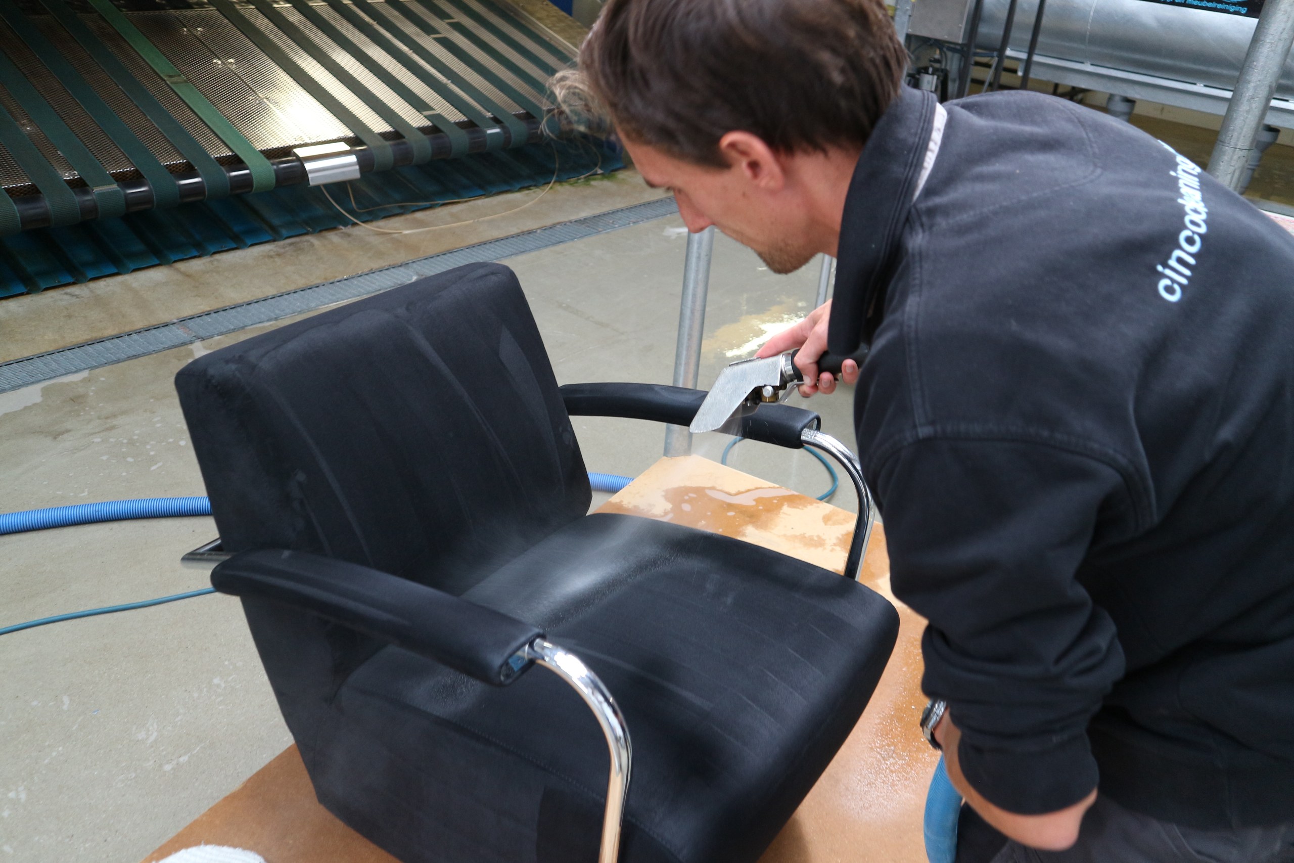 Medewerker reinigt zwarte stoffen fauteuil met sproei-extractie in werkplaats